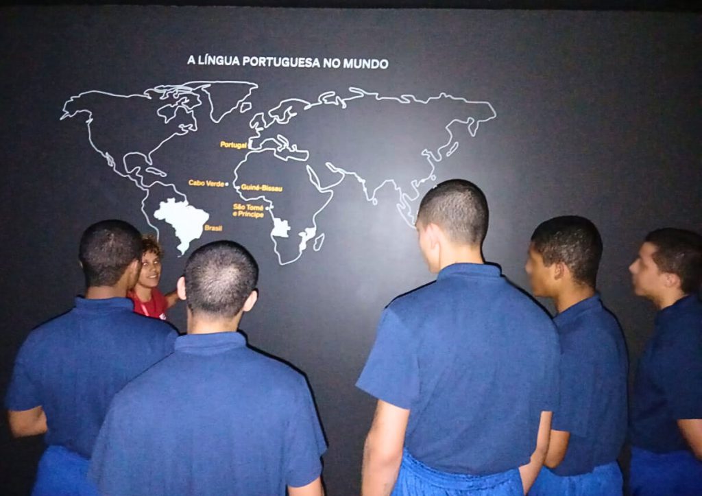 Jovens observam um mapa-múndi destacando os países de língua portuguesa em uma visita ao Museu da Língua Portuguesa.