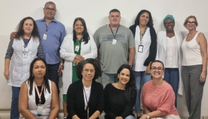 Foto mostra 11 adultos, entre homens e mulheres, posando para foto, estilo time de futebol: em pé há sete deles e quatro mulheres à frente, agachadas. São pessoas brancas, pardas e negras. Atrás deles há uma parede branca