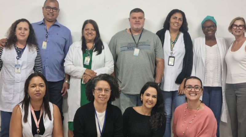 Foto mostra 11 adultos, entre homens e mulheres, posando para foto, estilo time de futebol: em pé há sete deles e quatro mulheres à frente, agachadas. São pessoas brancas, pardas e negras. Atrás deles há uma parede branca