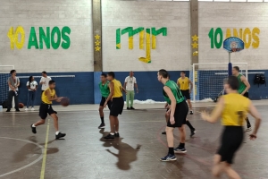 Foto mostra duas equipes de basquete formada por adolescente jogando na quadra do Instituto. Numa equipe, o uniforme é composto por camisa amarela e calção preto, enquanto a outra usa camisa verde a calção preto. Um jovem de camisa amarela bate a bola, indo na direção da cesta adversária, enquanto três adolescentes da equipe de camisa verde se posicionam em linha de defesa