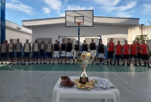 Foto mostra a premiação do regional do Torneio na quadra do centro de atendimento. Da esquerda para a direita aparecem ao fundo os adolescentes que compuseram as equipes perfilados: Guayí, Terra Nova e Guarulhos. Atrás dos jovens aparecem a tabela de basquete e uma edificação. Em primeiro plano, à frente dos jovens, está uma mesa com medalhas e o troféu. O dia está ensolarado, com céu com poucas nuvens.