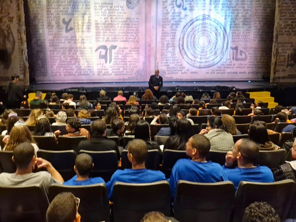 Plateia do Teatro Renault com jovens de uniforme azul aguardando o início do espetáculo Wicked.