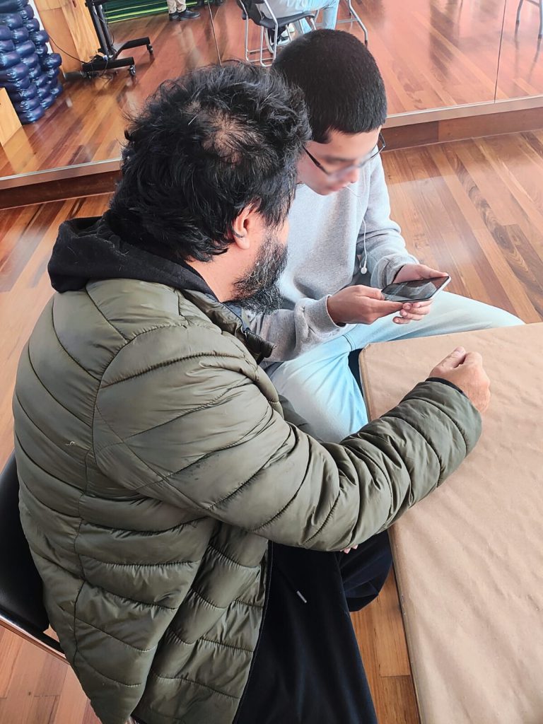 Educador e jovem sentados lado a lado olham para um celular durante atividade prática.