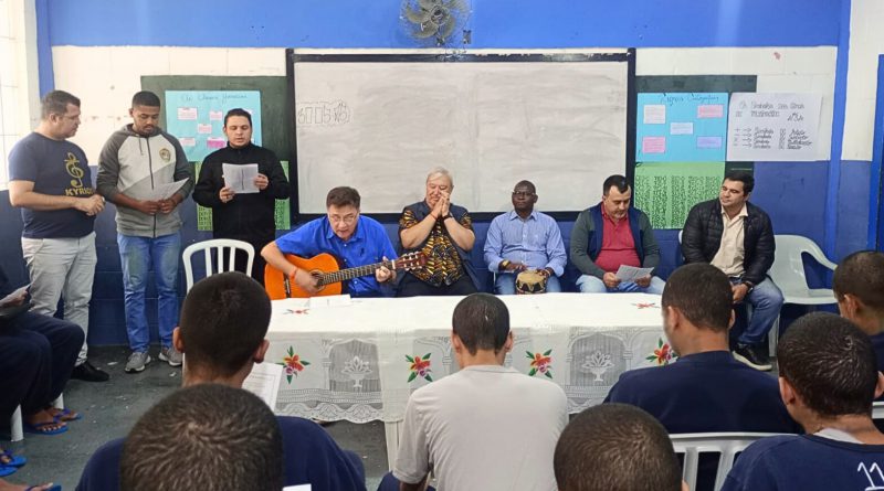 Grupo da Fazenda da Esperança canta e toca instrumentos para adolescentes sentados em uma sala no CASA.