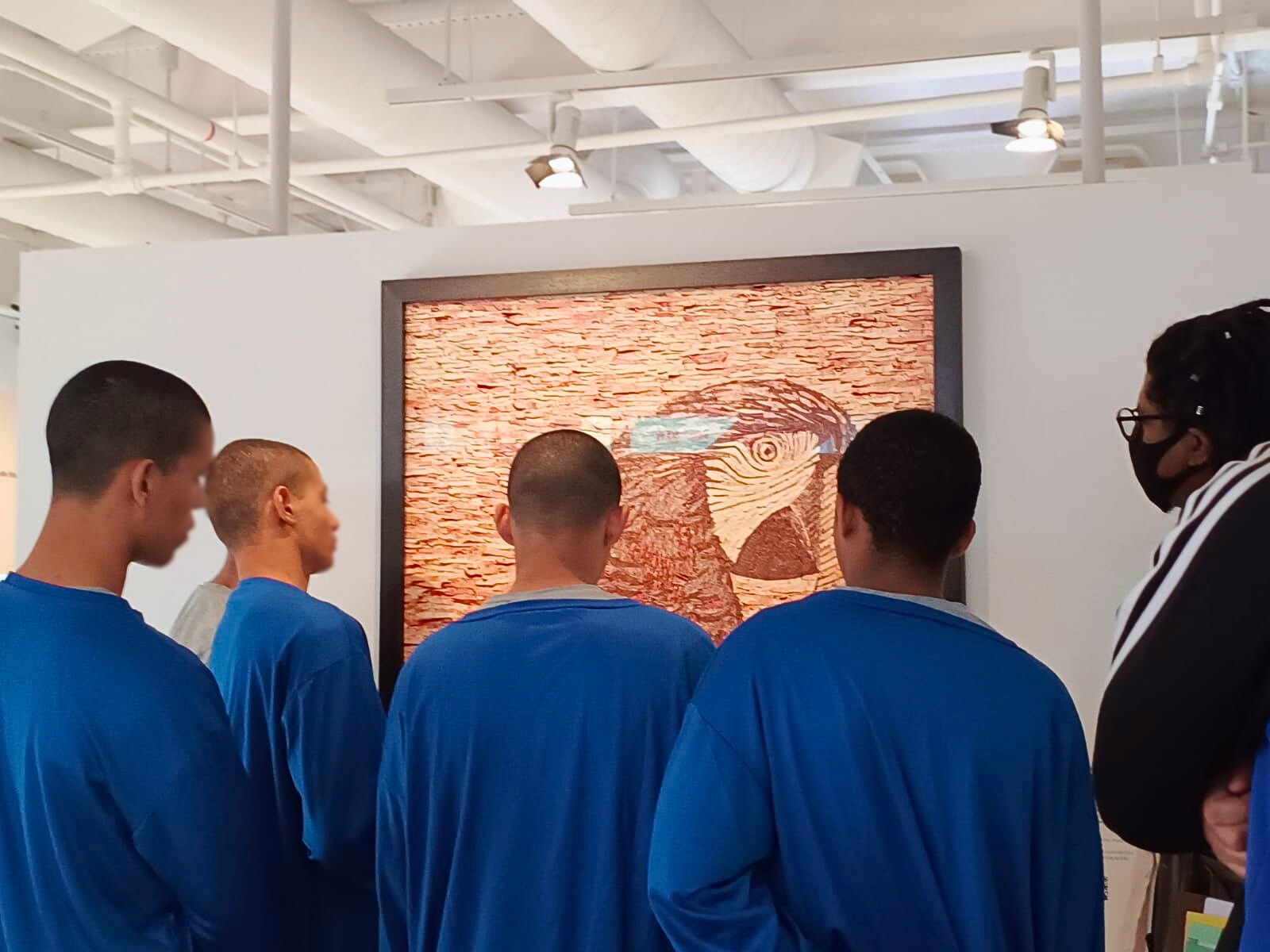 Adolescentes observam atentamente uma obra de arte que retrata um pássaro, feita com cédulas fragmentadas.
