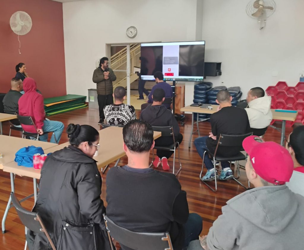 Adolescentes sentados assistem a uma apresentação de conteúdo audiovisual em uma sala de aula.
