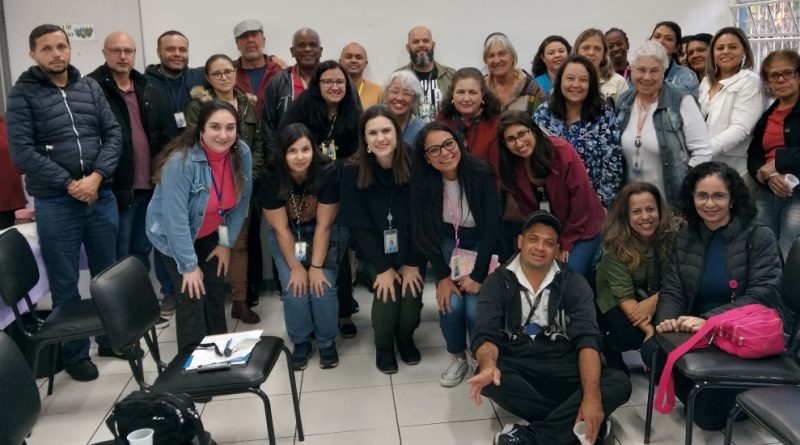 Foto mostra 31 adultos, entre homens e mulheres, numa sala fechada de paredes brancas e com cadeiras dispostas no piso. Eles estão um ao lado do outro, posando para a foto