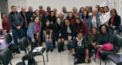 Foto mostra 31 adultos, entre homens e mulheres, numa sala fechada de paredes brancas e com cadeiras dispostas no piso. Eles estão um ao lado do outro, posando para a foto