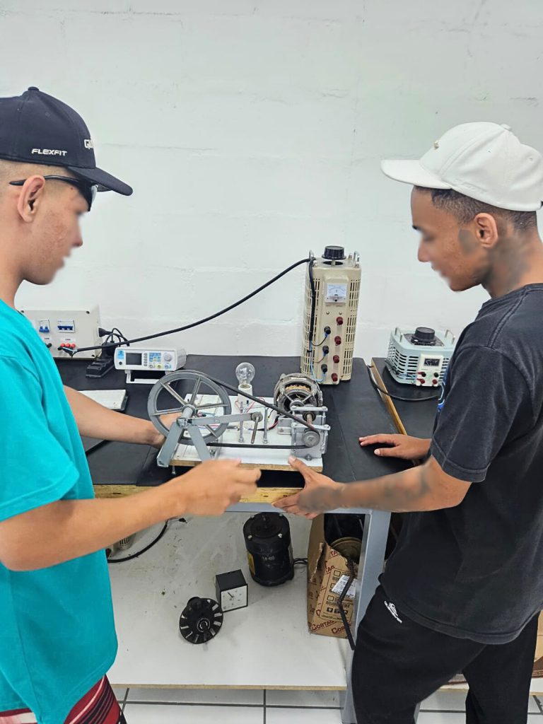 Dois adolescentes manipulam um equipamento de experimento técnico sobre uma bancada em um laboratório.