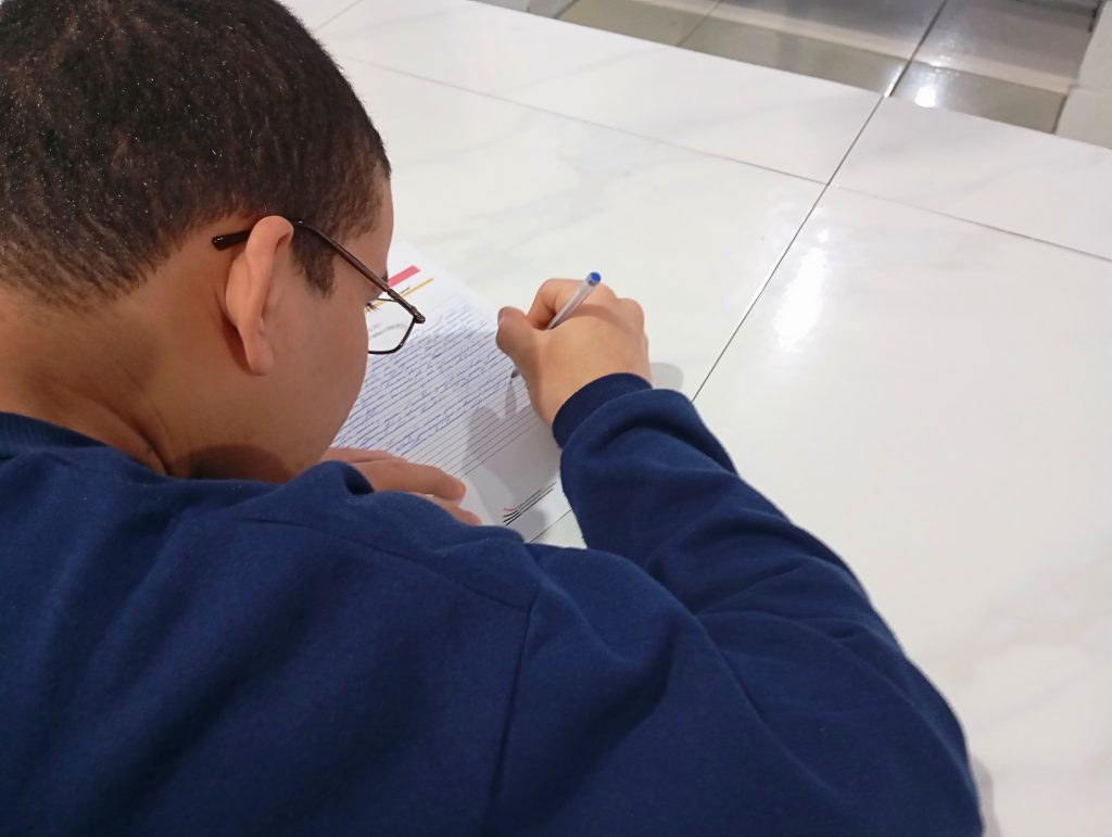 Adolescente da Fundação CASA escreve à mão sua redação durante o concurso China-Brasil